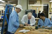 Two craftsman observe a guest trying his hand at frame restoration